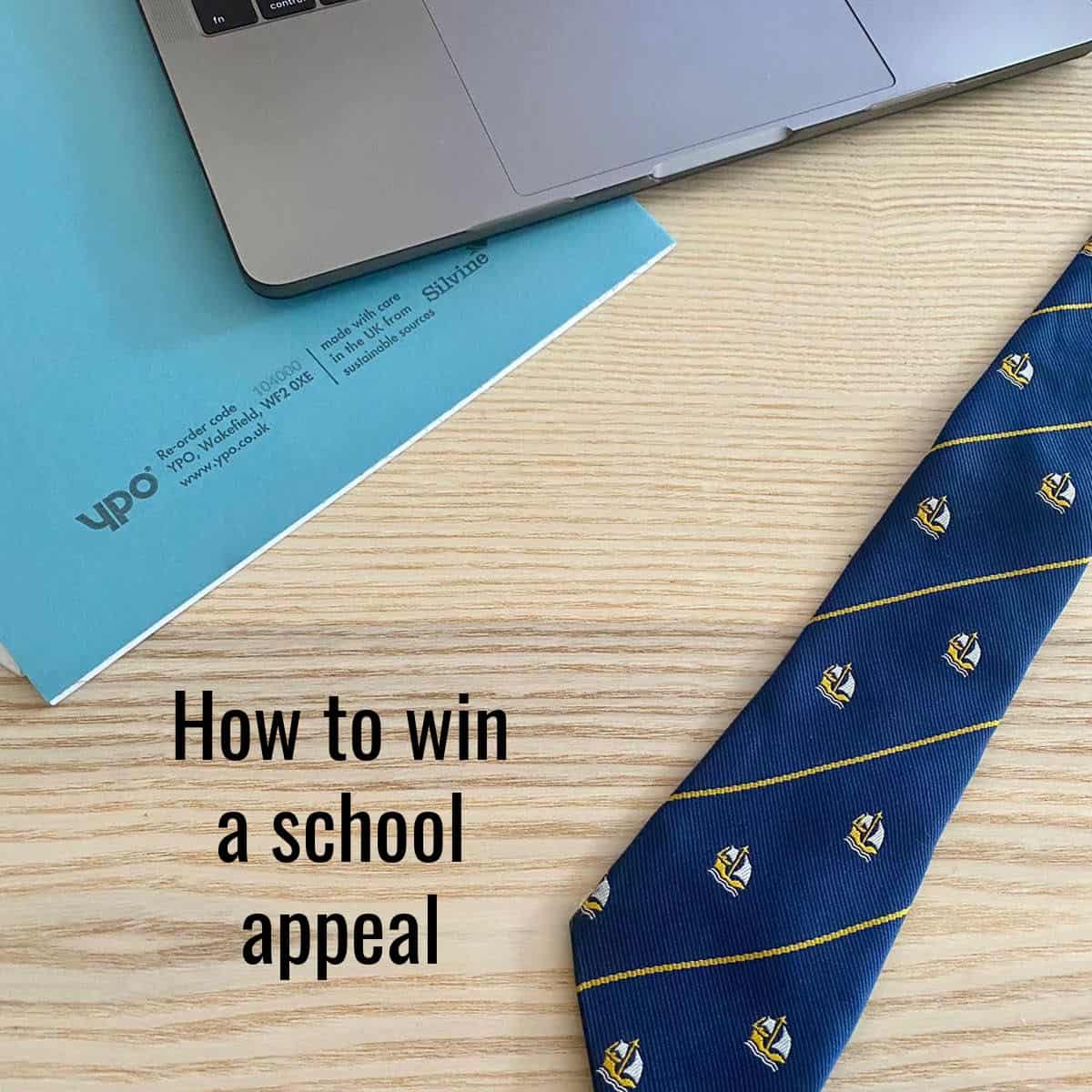navy tie on a wooden desk with a blue notepad and the corner of a laptop