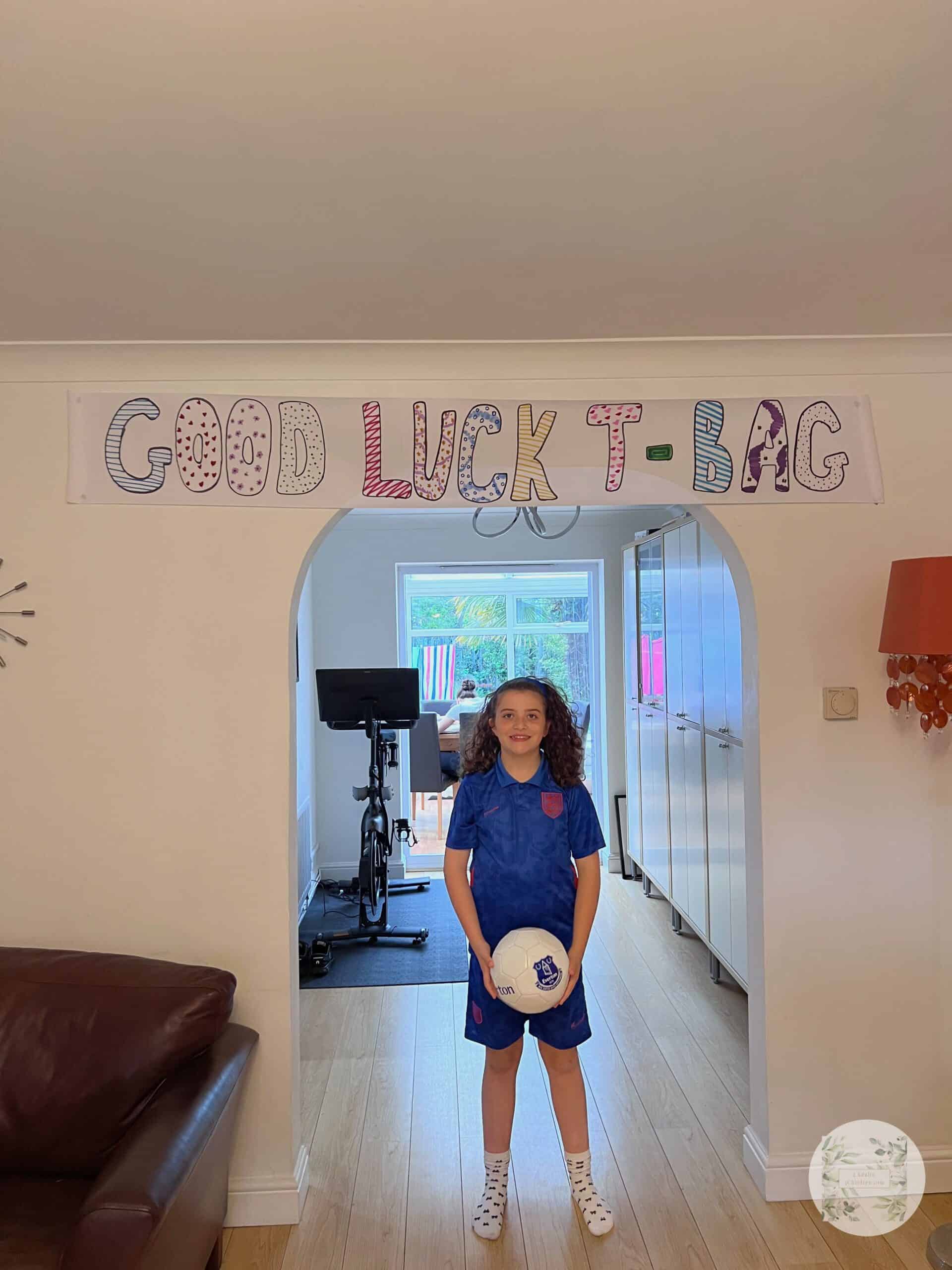 Picture of young girl in football kit in front of a good luck sign