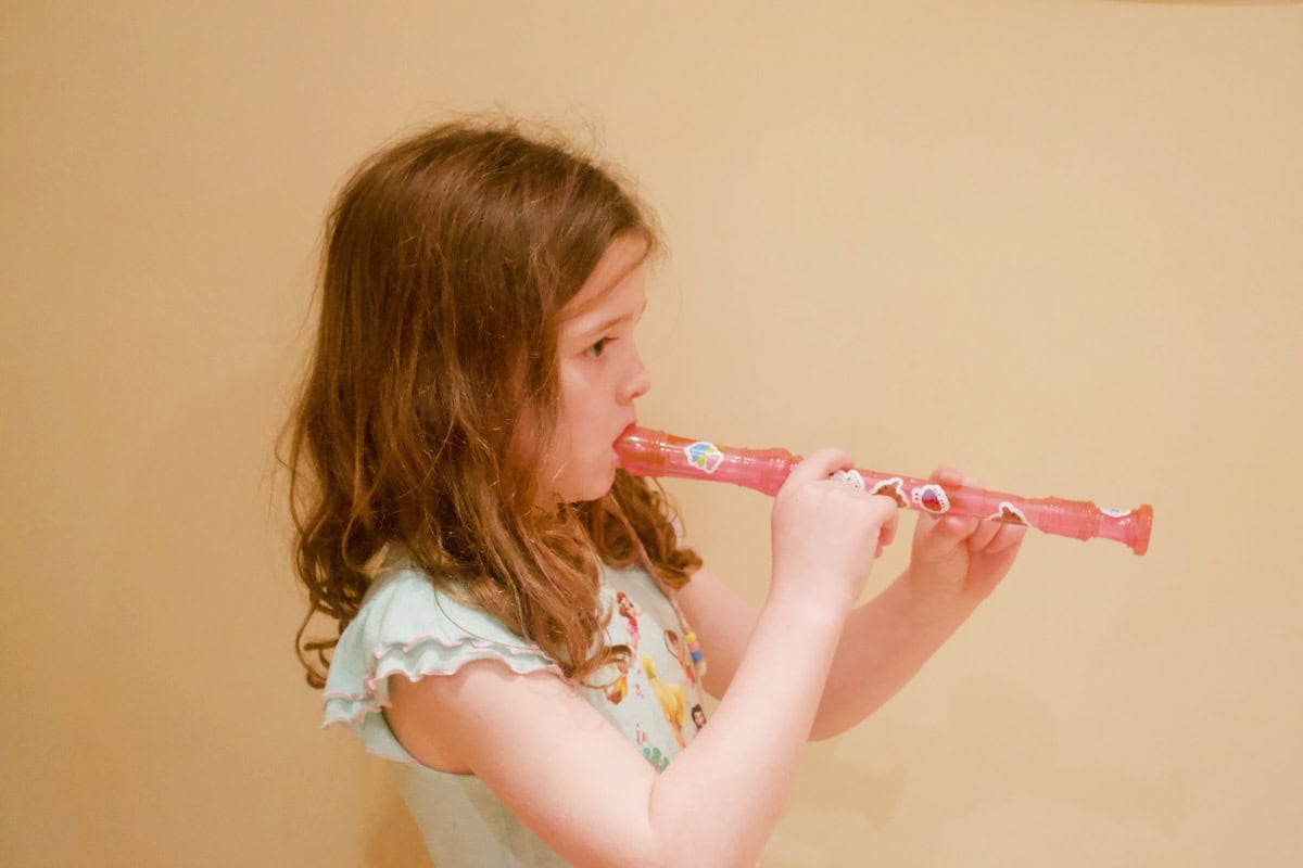 girl with dark hair and a pale green dress playing a pink recorder with stickers on it