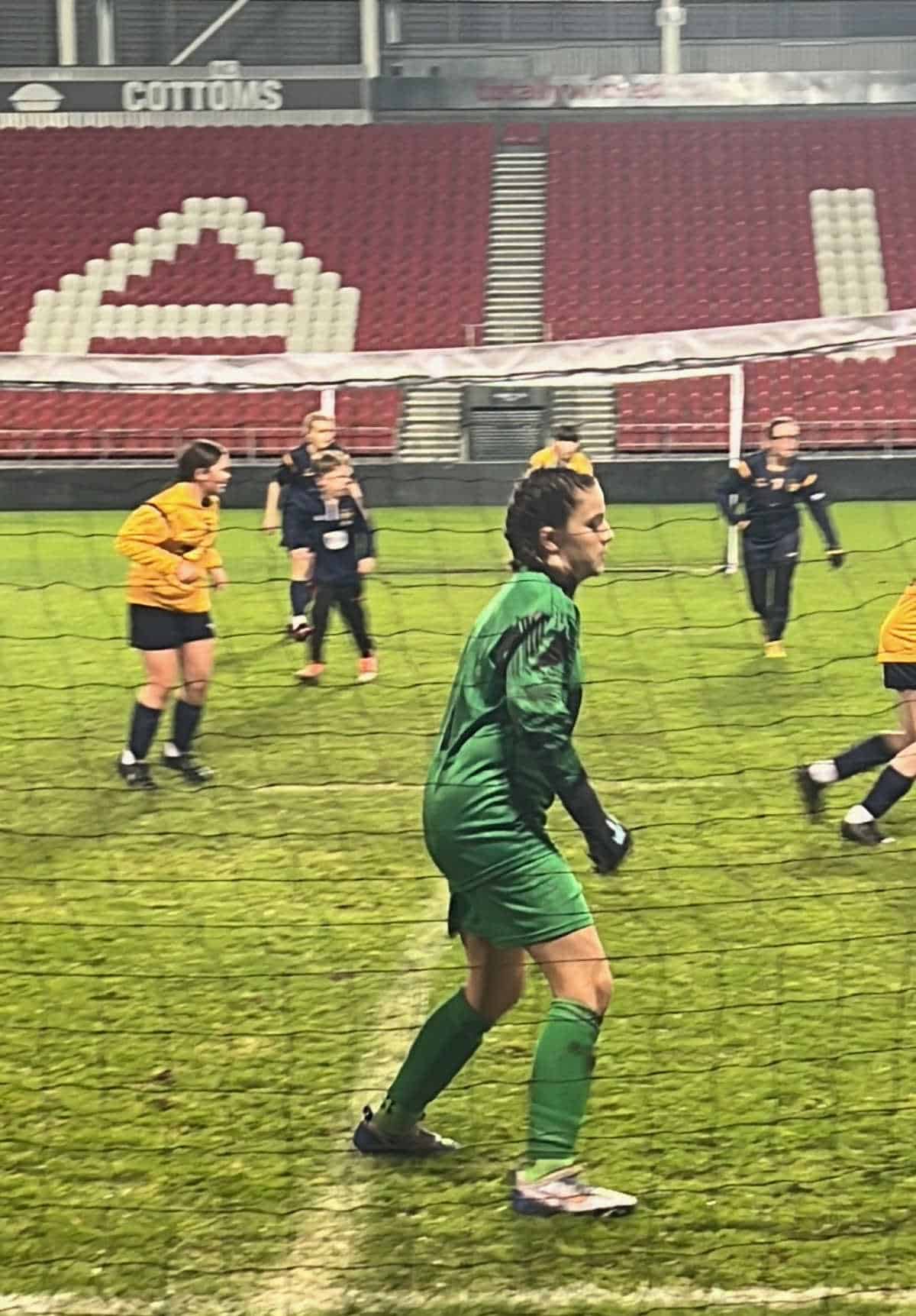 girl on a football pitch wearing a green kit