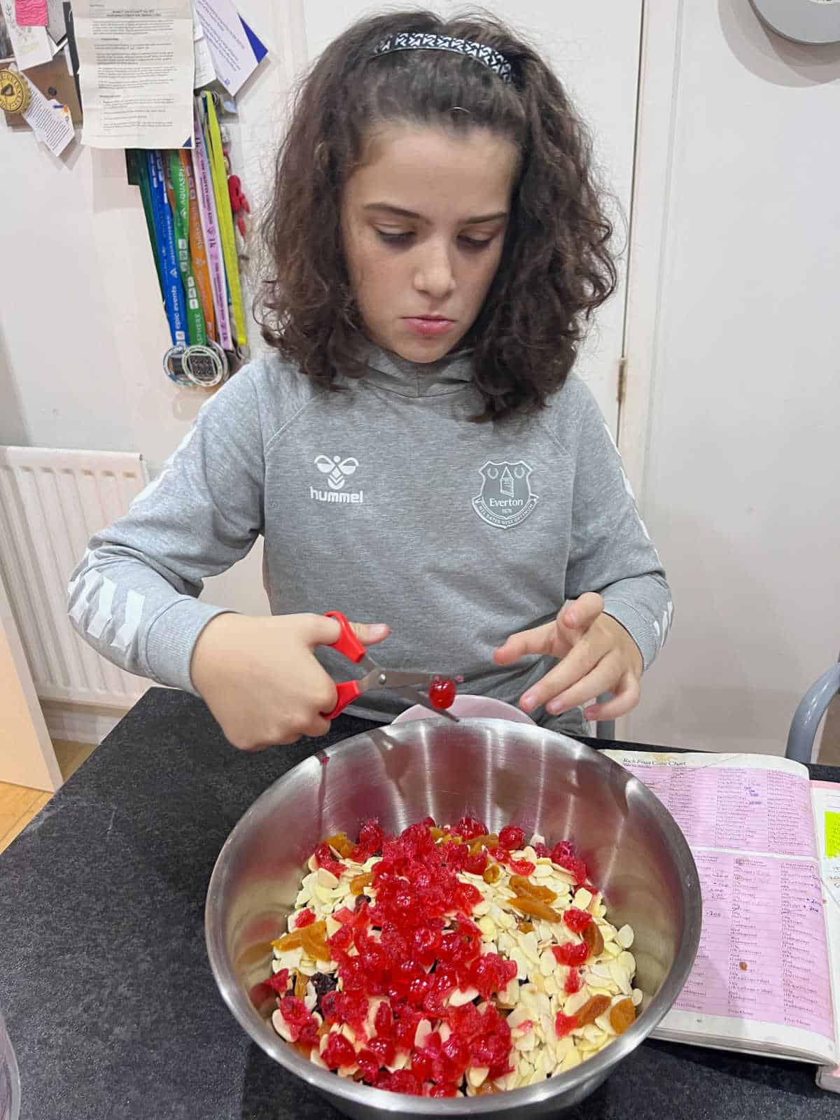 girl wearing a grey Everton hoodie chopping cherries in a large metal bowl