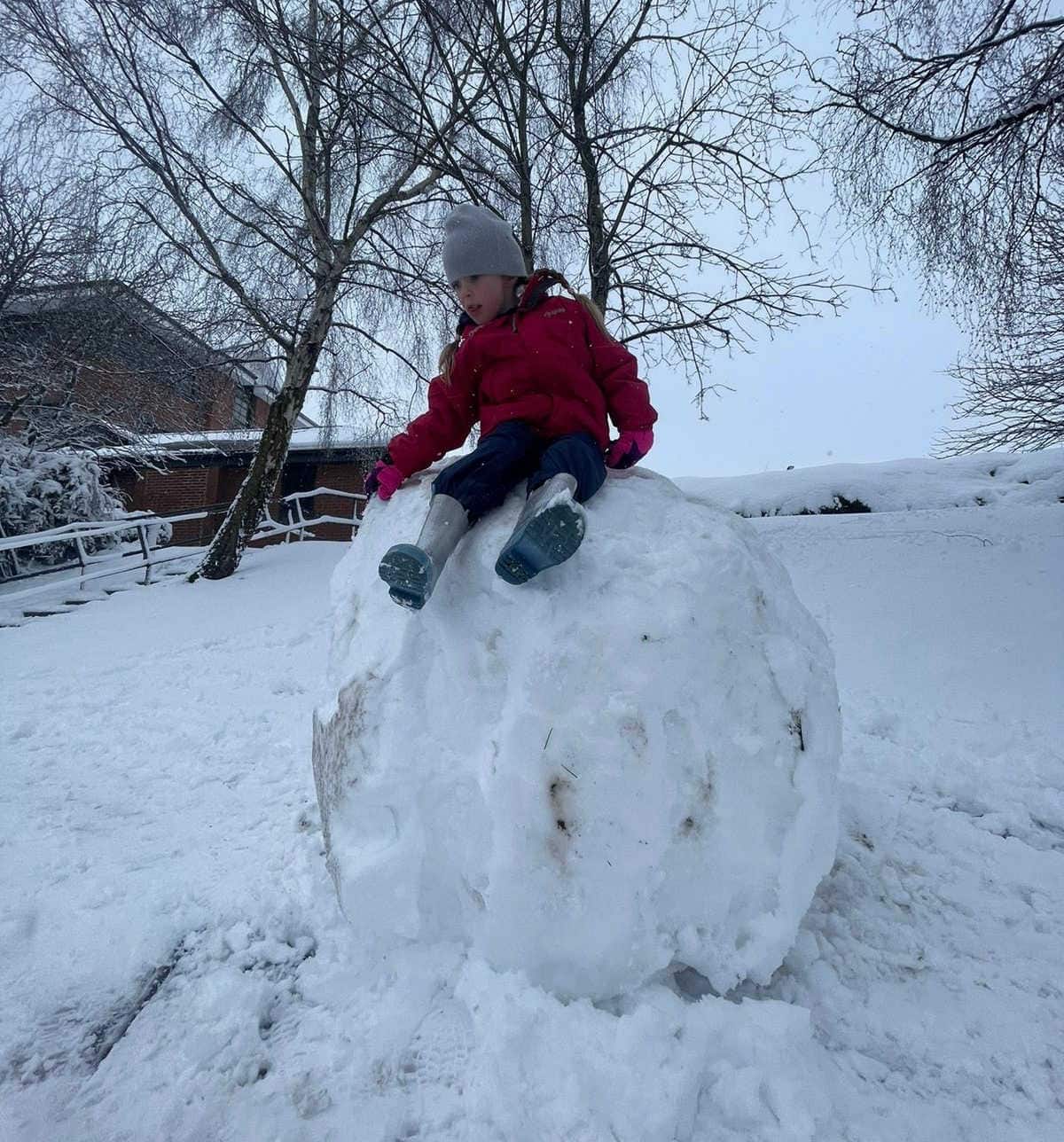 girl in a red coat sat on top of a giant snowball