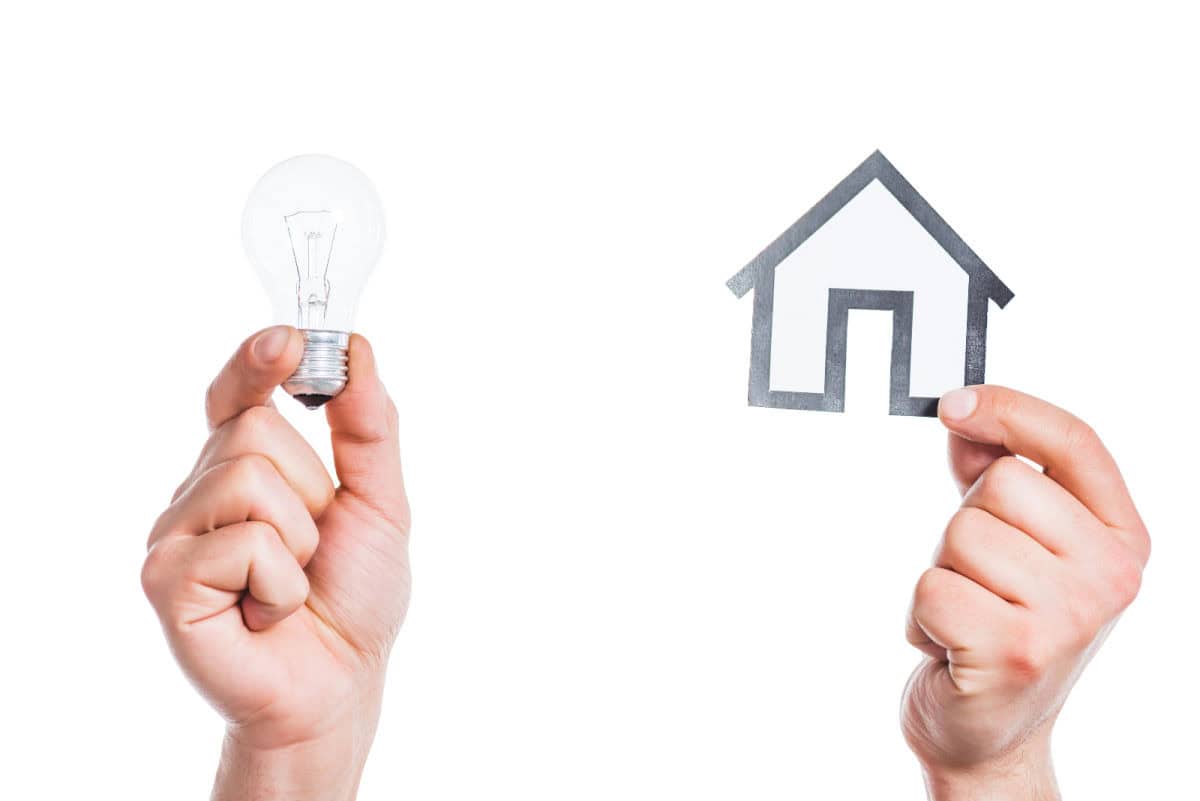 2 hands against a white background - one is holding up a light bulb and the other is holding up the outline of a house