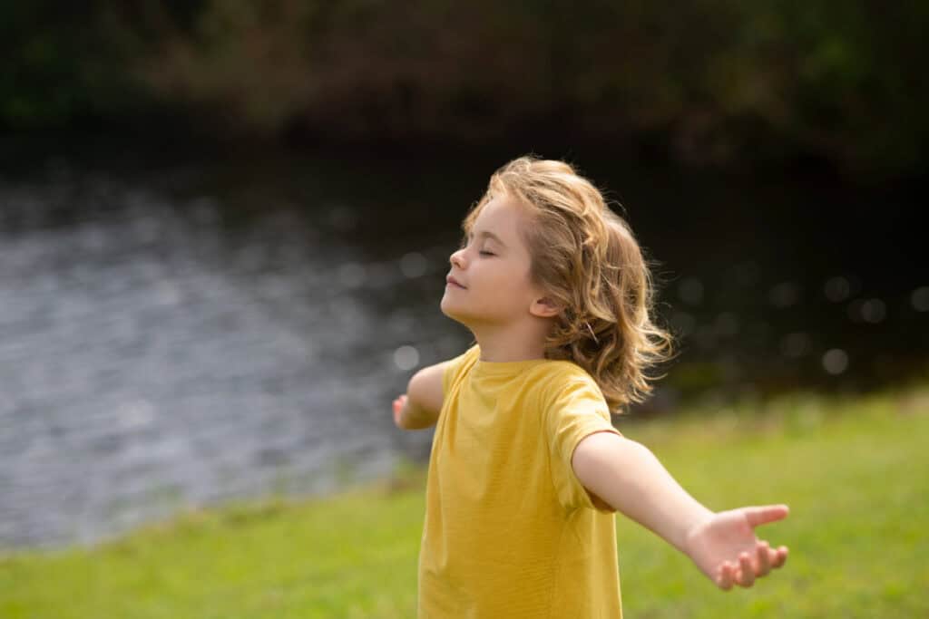 young girl wearing a yellow t shirt in a field with arms outstretched practising a fun mindfulness activities to help mental health